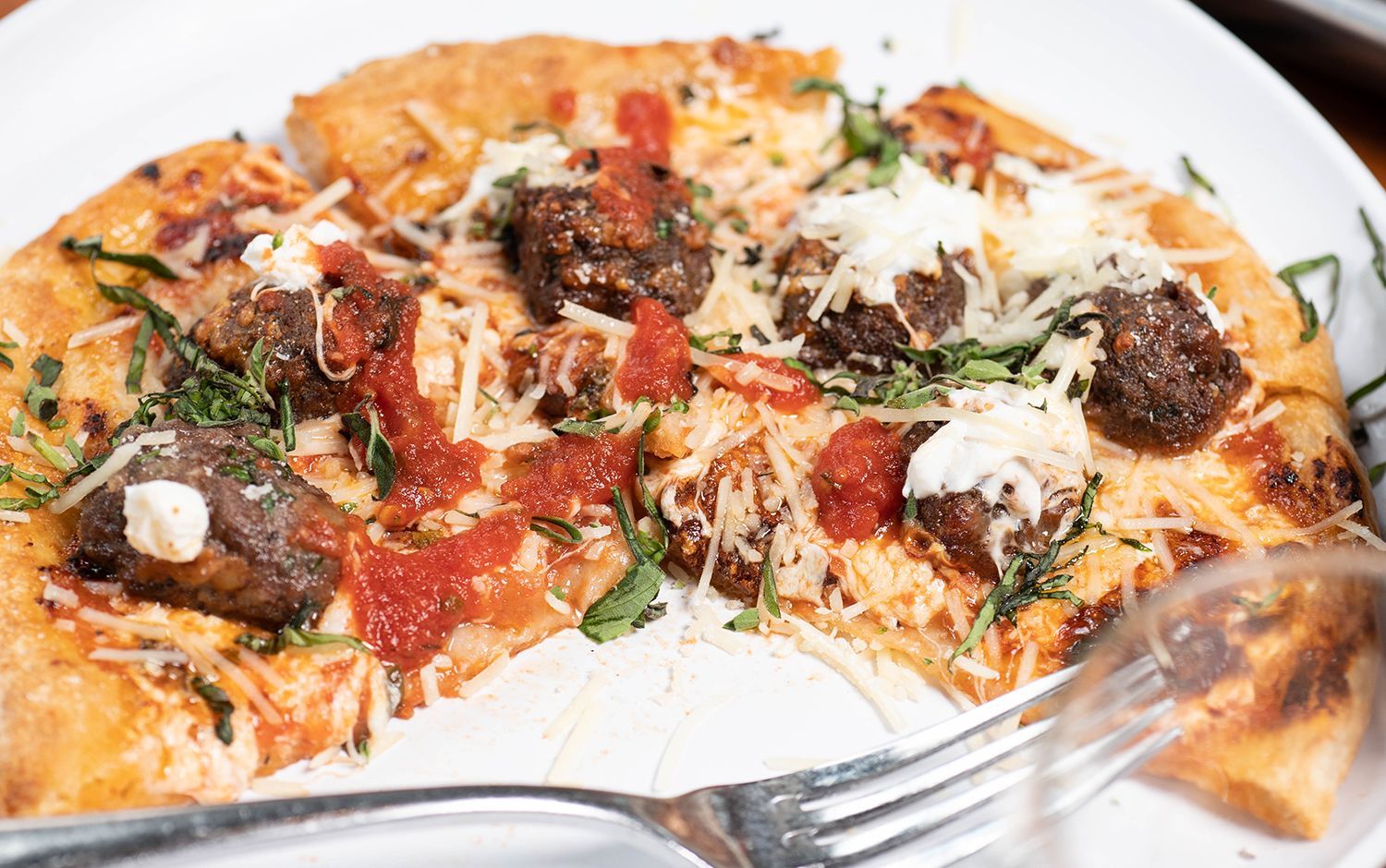 A pizza with meatballs and cheese on a white plate with a fork.