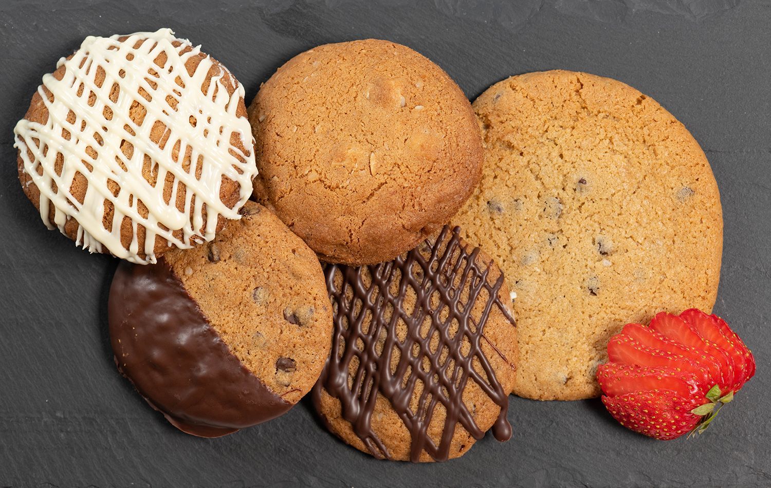Four different types of cookies are on a table with a strawberry