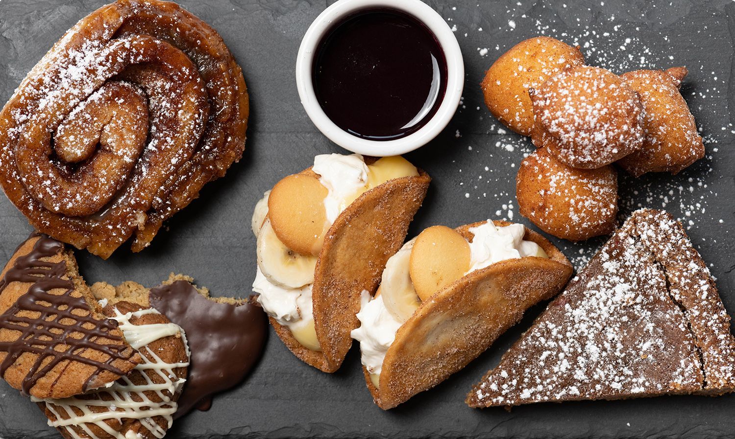 A variety of desserts on a table with a bowl of syrup