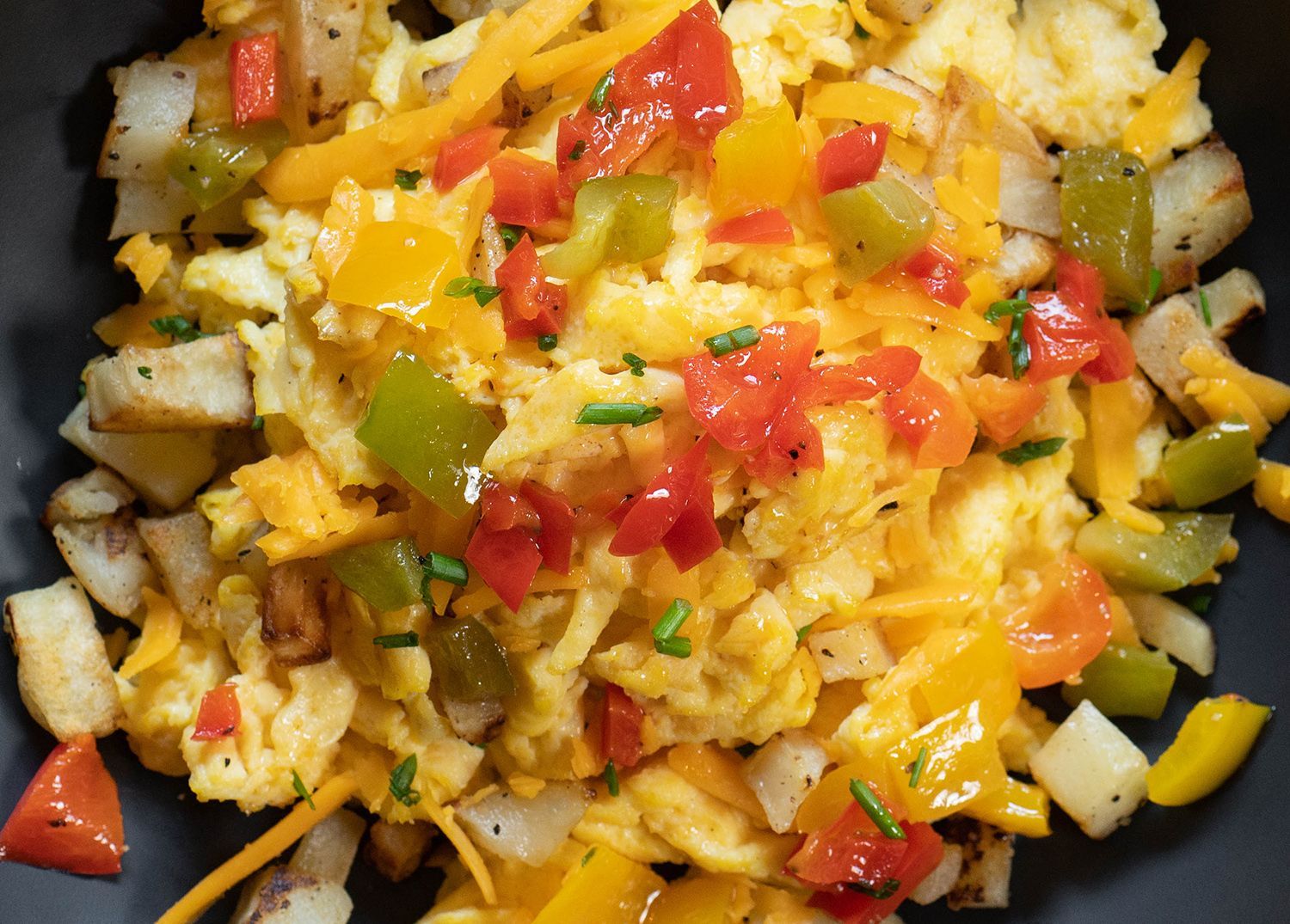 A close up of a plate of food with eggs , potatoes , peppers and cheese.