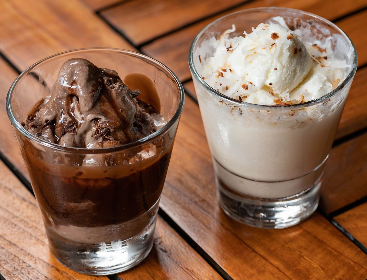 Two glasses of ice cream are sitting on a wooden table.