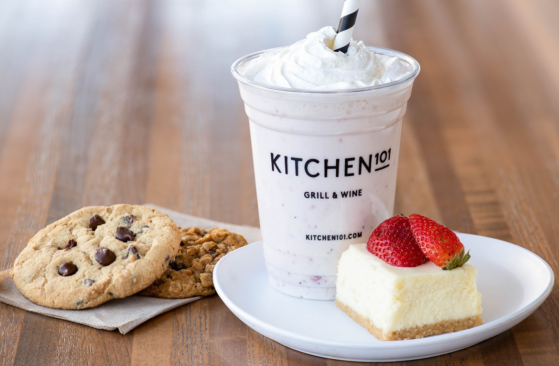 A cup of milkshake , a cookie , and a piece of cheesecake on a plate.