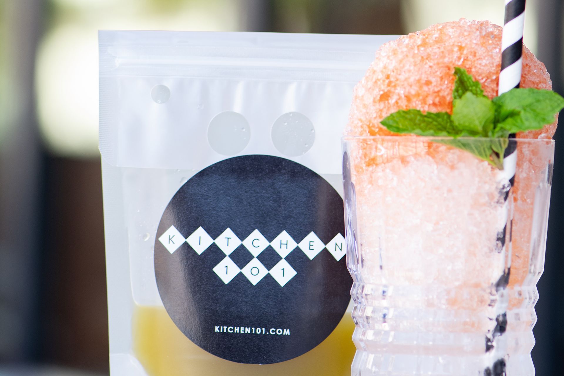 A bag of ice cubes is next to a glass of iced tea with a straw.