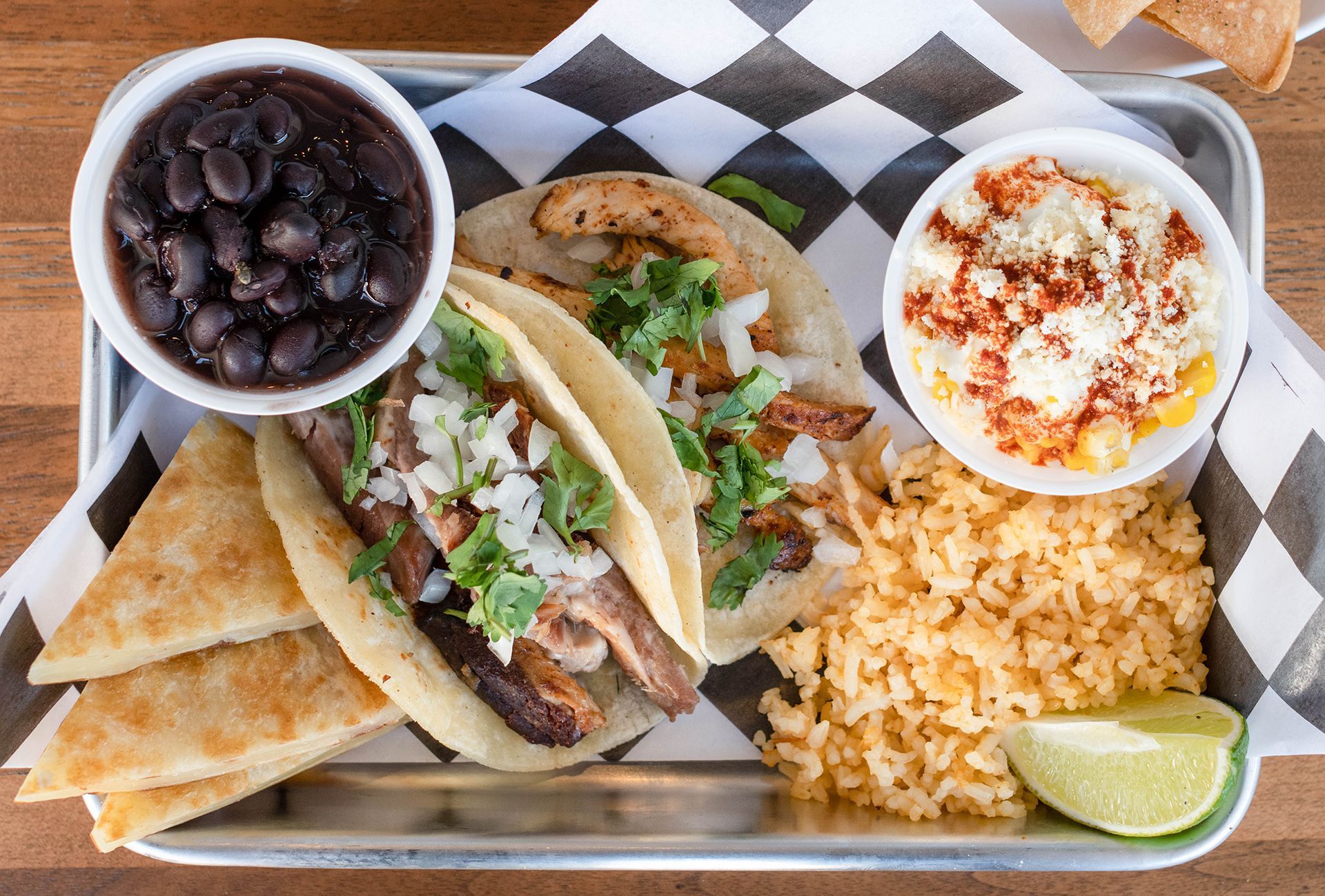 A tray of food with tacos , rice , beans and corn on the cob.