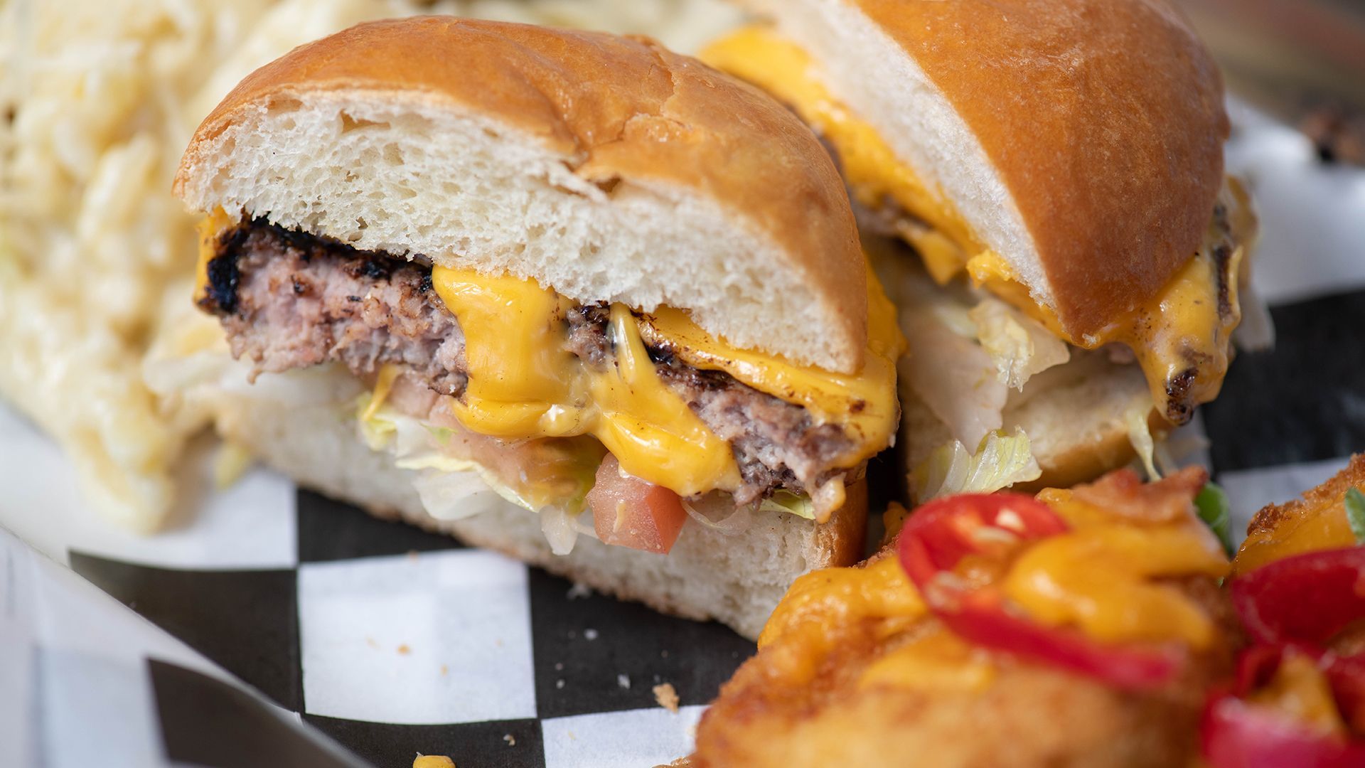 A close up of a hamburger and macaroni and cheese on a checkered plate.