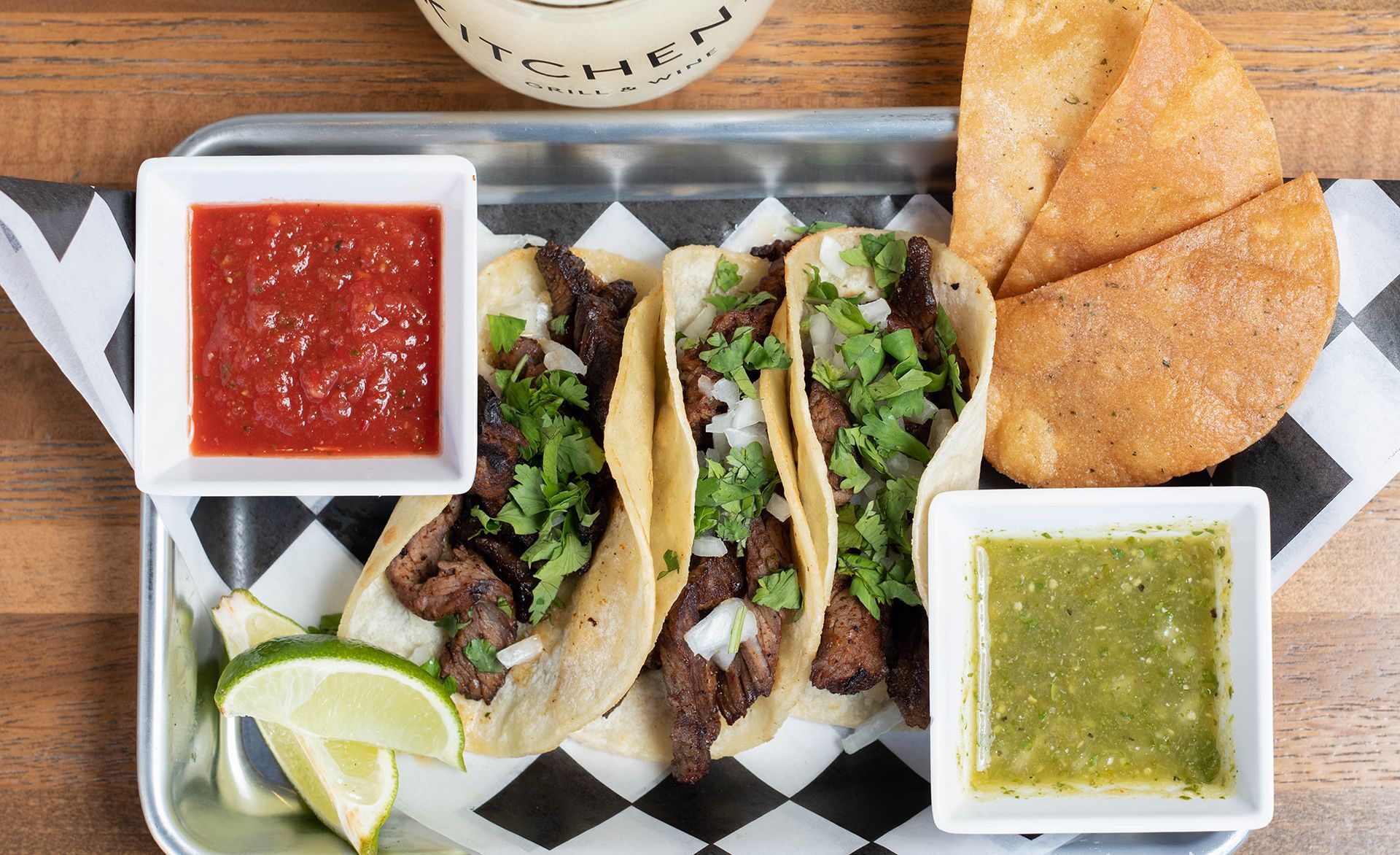 A metal tray filled with tacos , salsa , and tortilla chips.