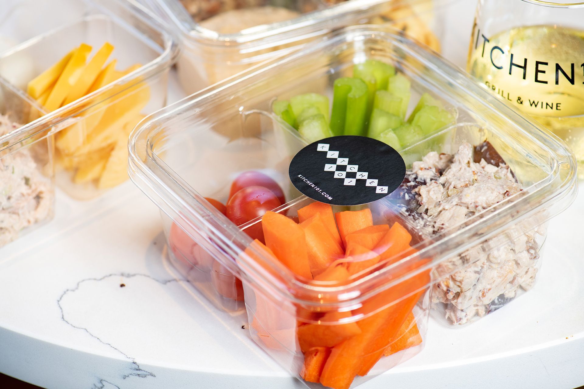 A plastic container filled with carrots , celery , grapes and tuna on a table.