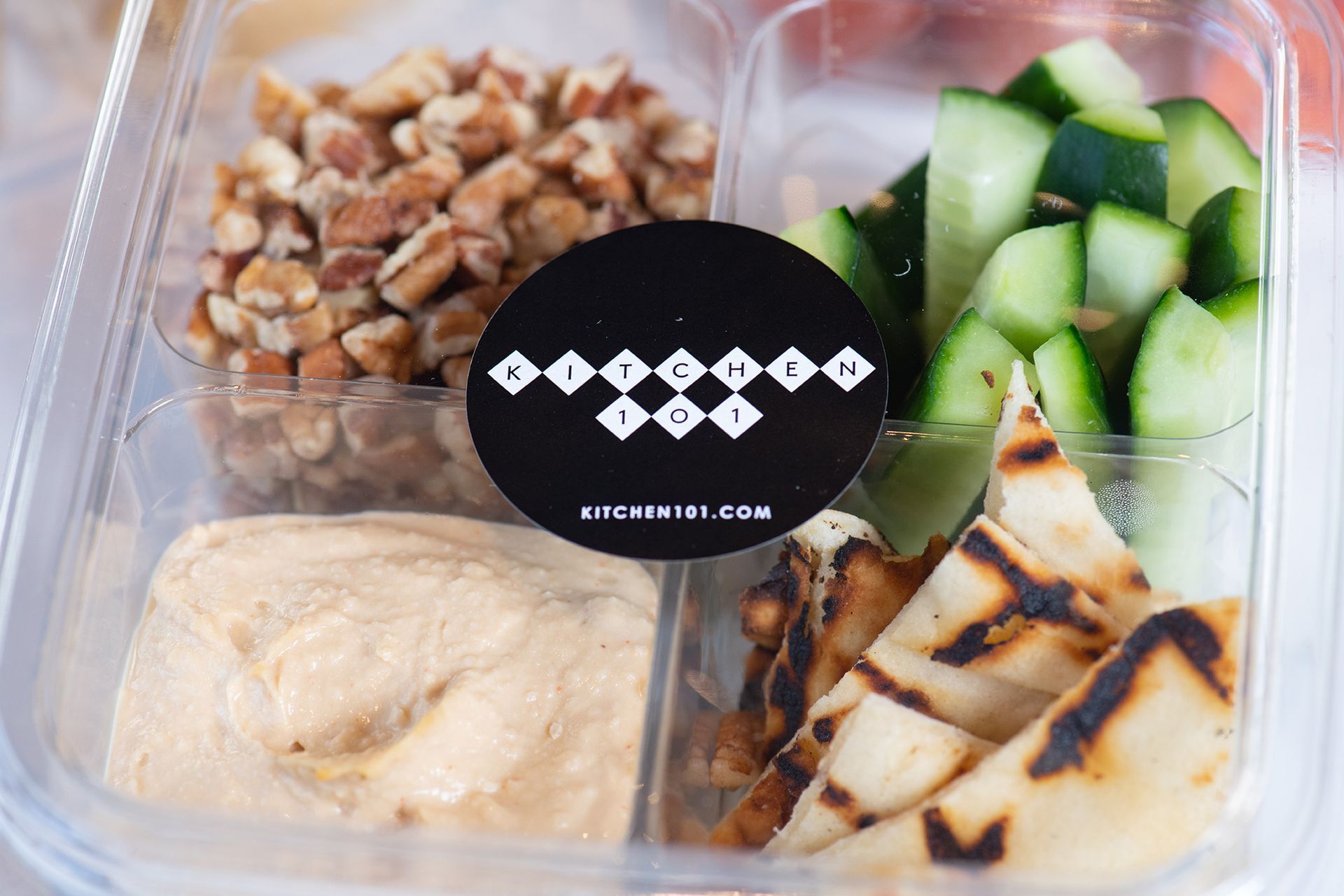 A plastic container filled with nuts , cucumbers , and pita bread.