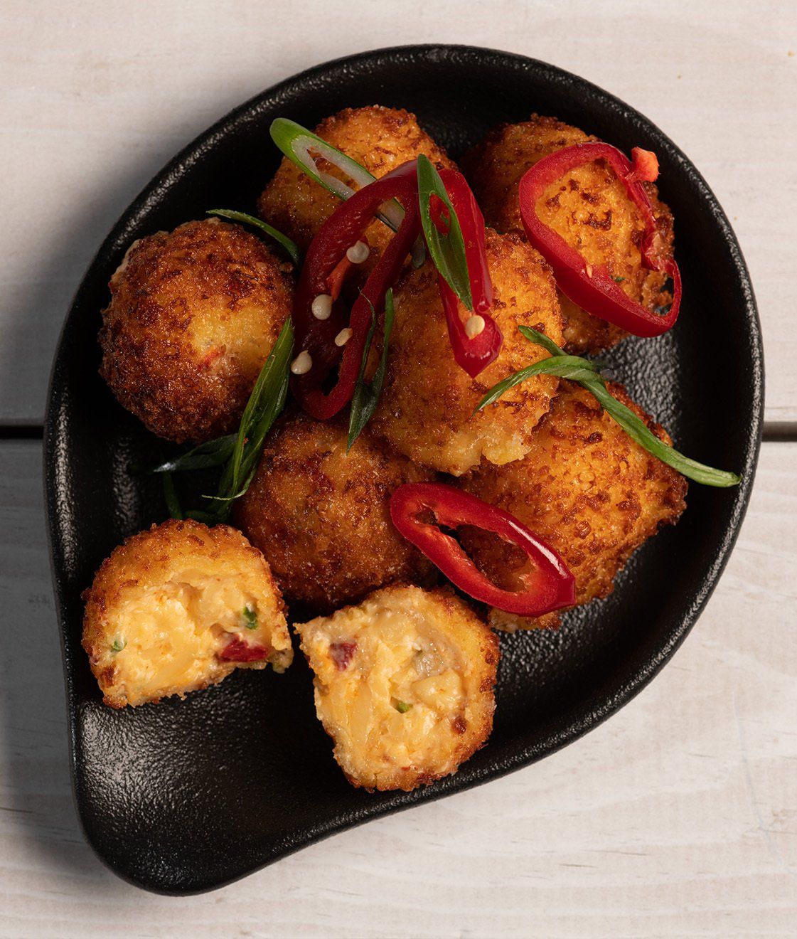 A black plate topped with fried food with red peppers and green onions