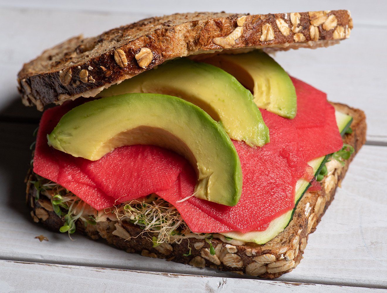 A close up of a sandwich with avocado and red meat on a table.