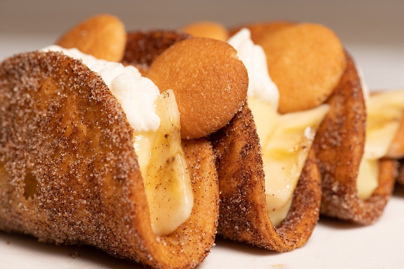 A close up of three tacos with banana pudding and whipped cream on a white plate.