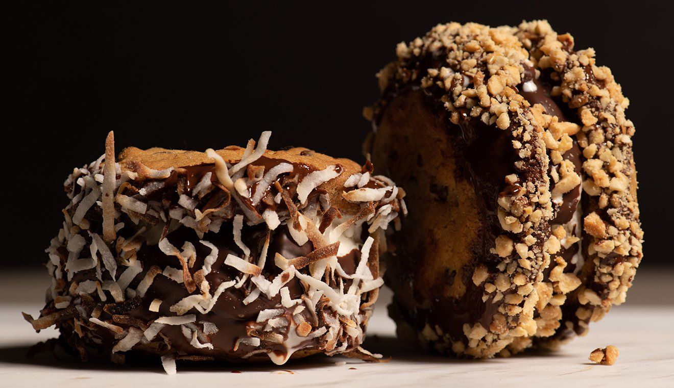 Two chocolate covered donuts with coconut and nuts on a table.