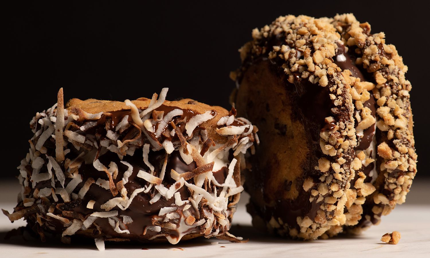 Two chocolate covered donuts with coconut and nuts on a table.