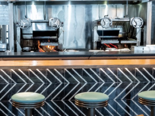 A restaurant kitchen with a bar and stools in front of it.