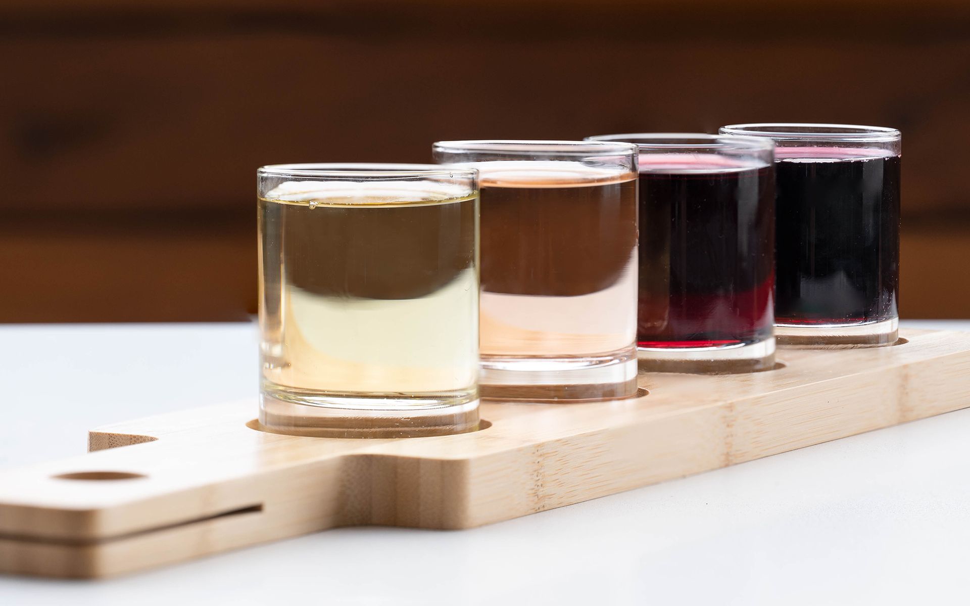 A row of shot glasses filled with different colored liquids on a wooden tray.