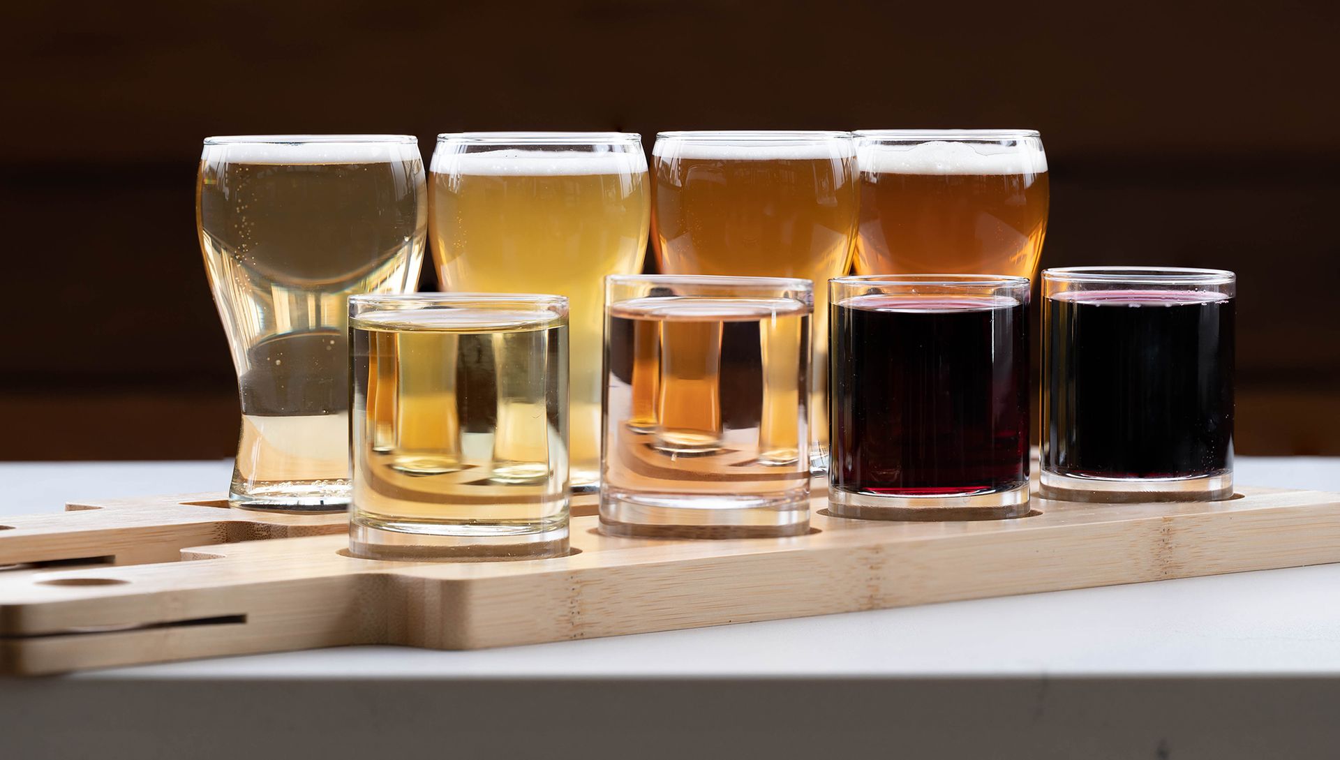 A wooden cutting board topped with glasses of different types of beer.