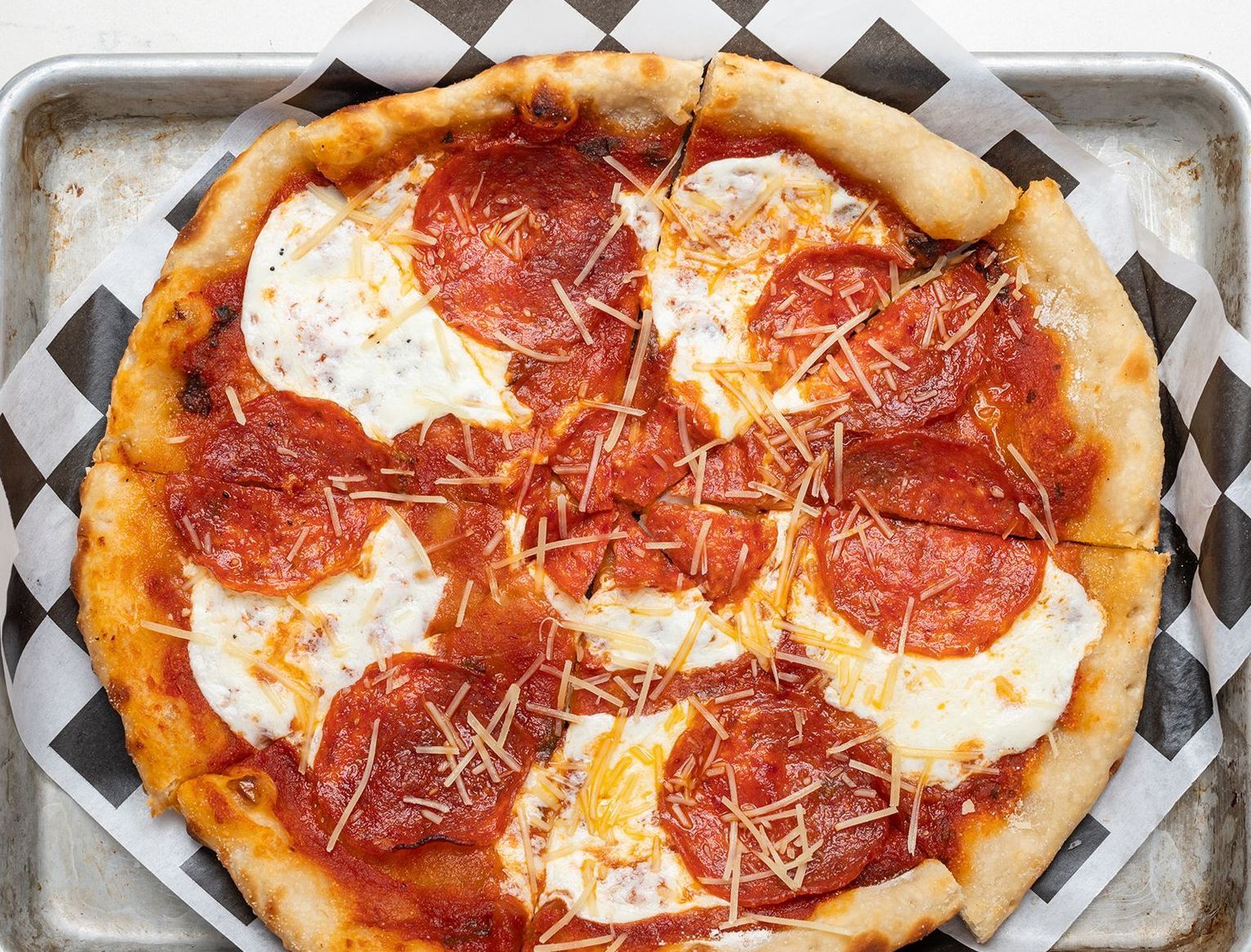 A pepperoni pizza is sitting on a checkered paper on a pan.