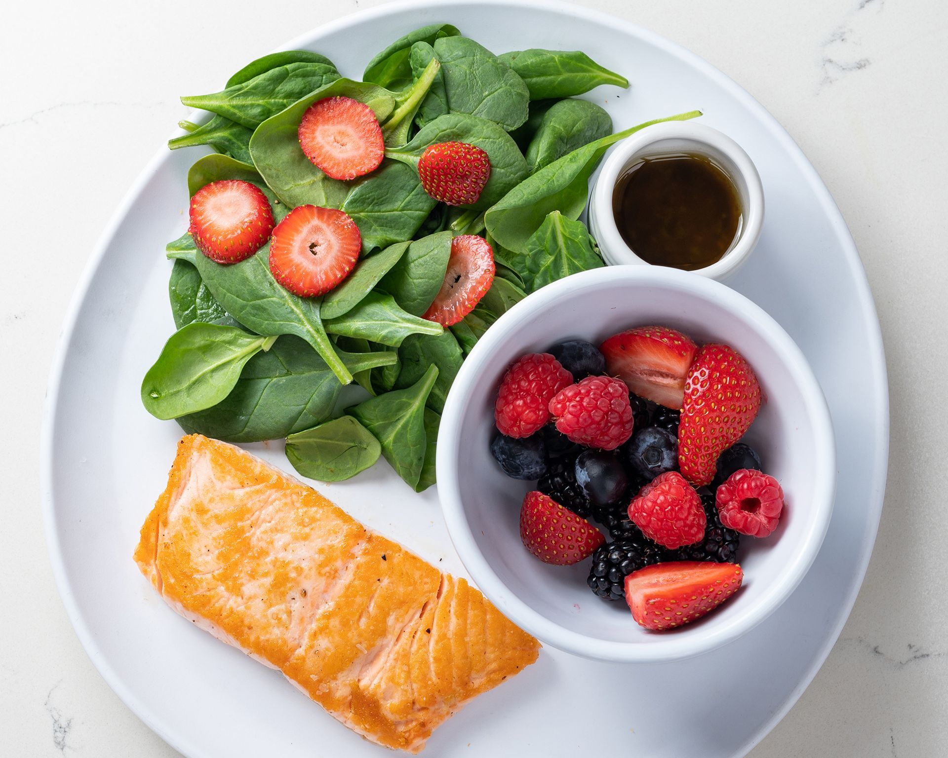 A white plate topped with salmon , spinach , strawberries and raspberries.