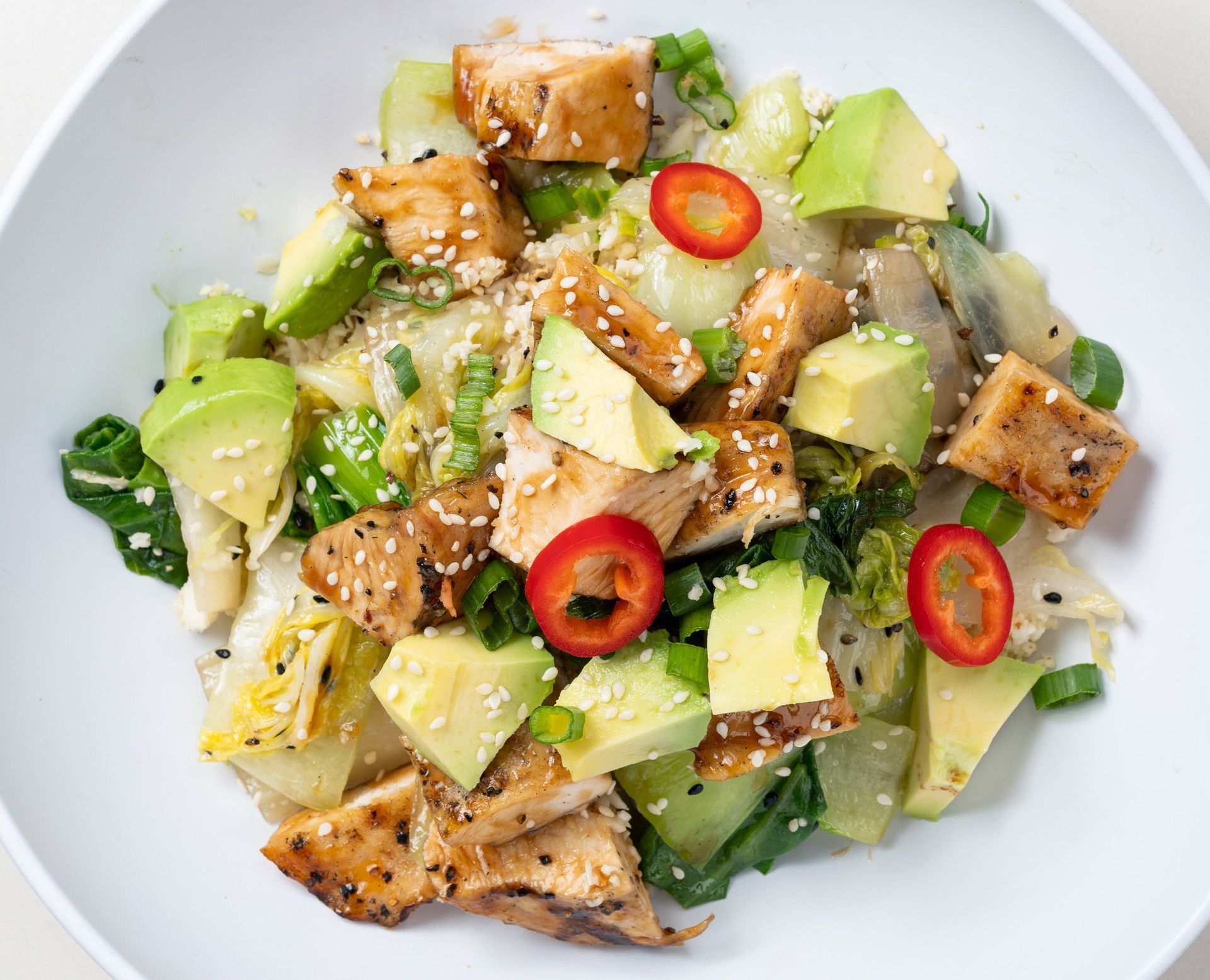 A salad with chicken , avocado , red peppers and sesame seeds on a white plate.