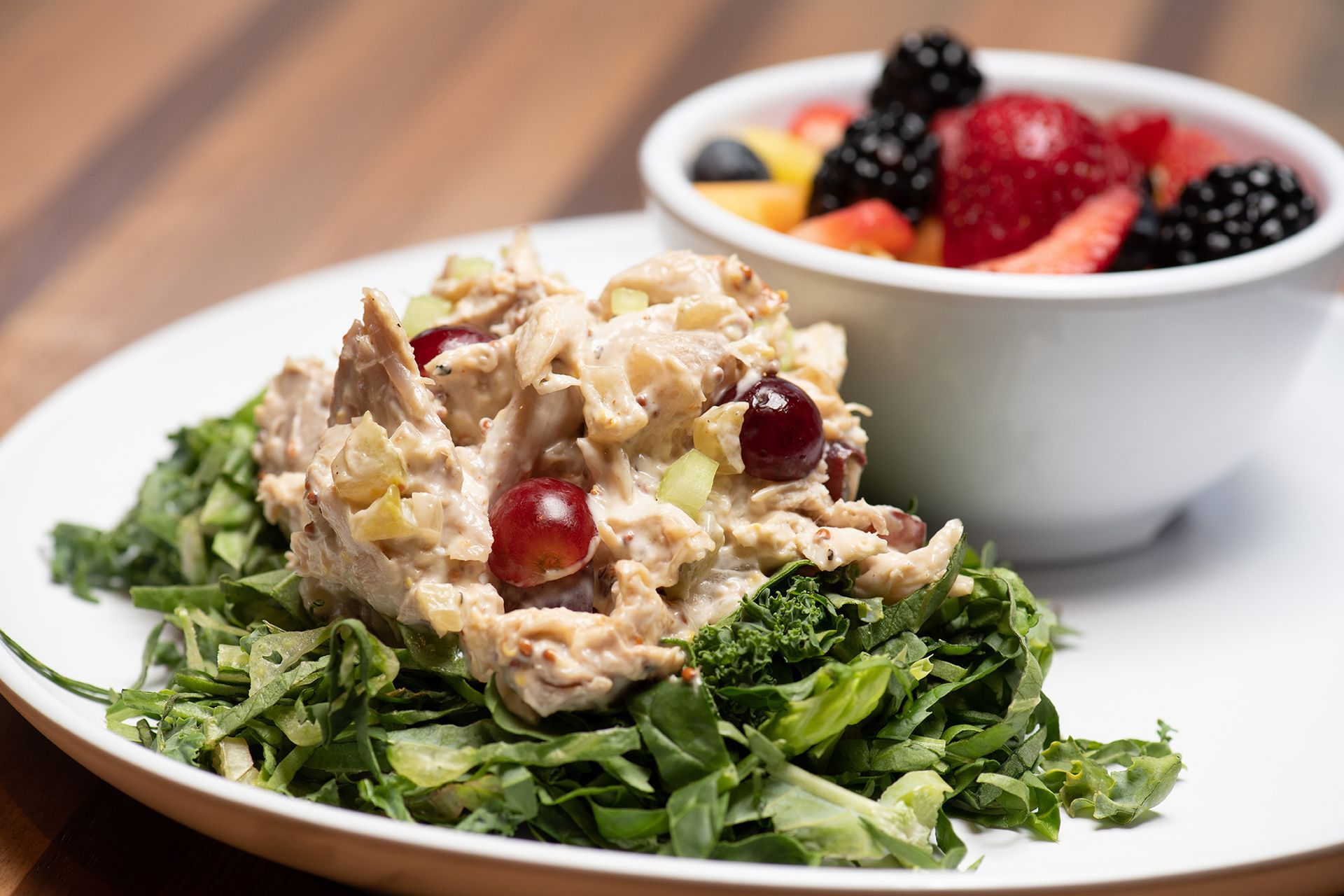 A white plate topped with a salad and a bowl of fruit.