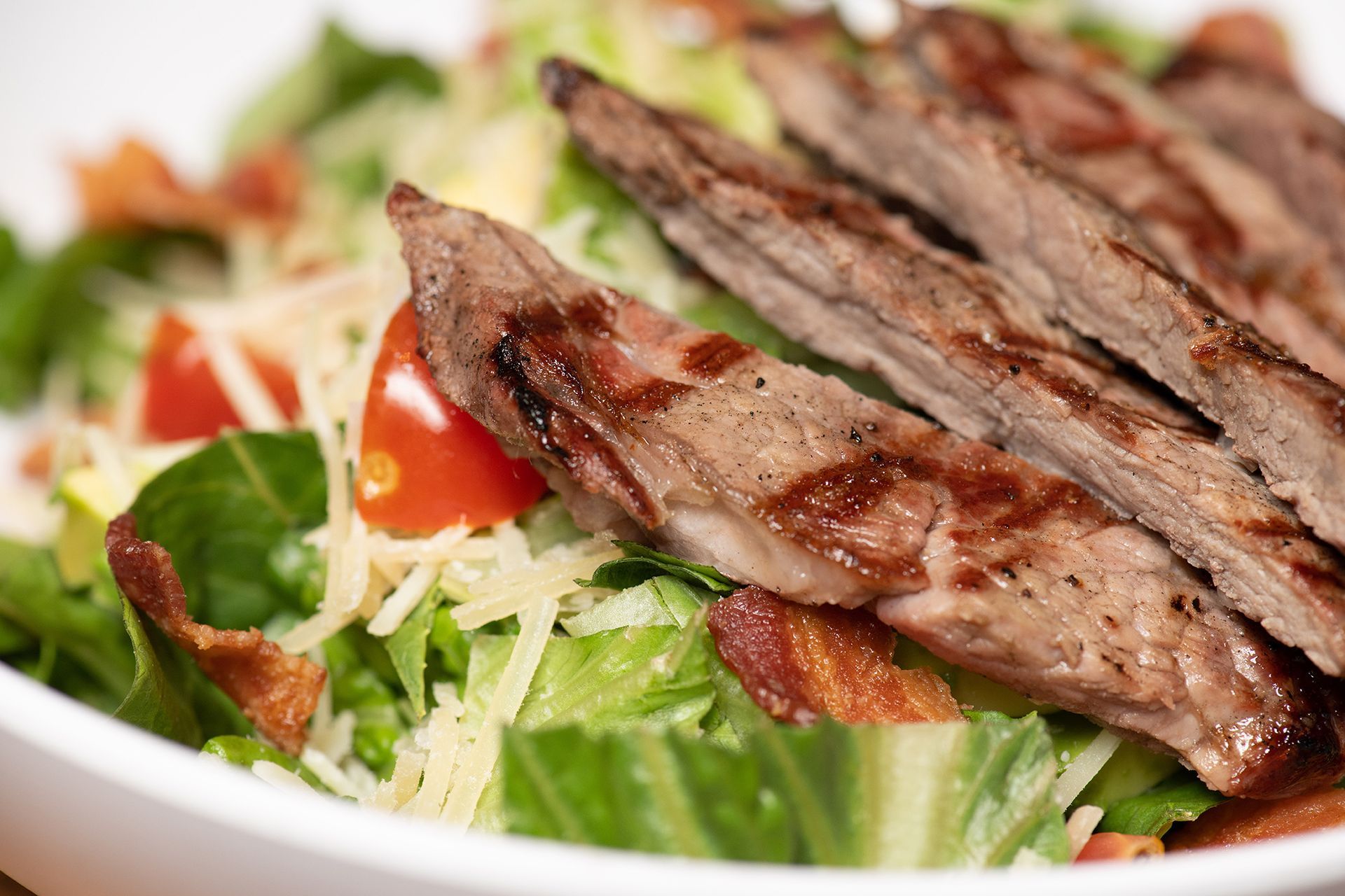 A close up of a salad with steak , lettuce , tomatoes and bacon.