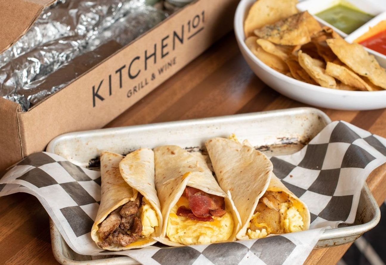 Three burritos are sitting on a plate next to a bowl of chips.