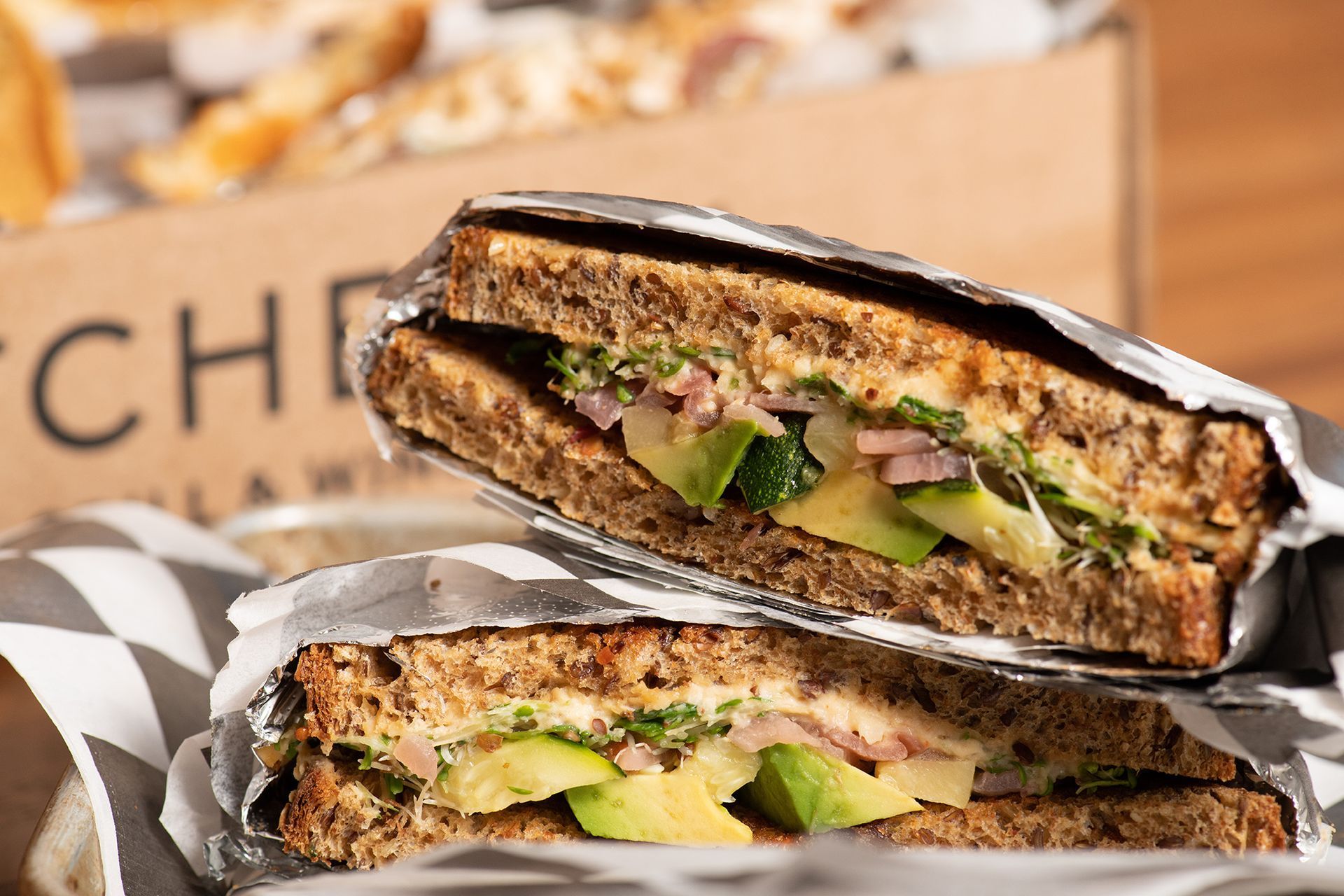 A close up of a sandwich wrapped in tin foil on a table.