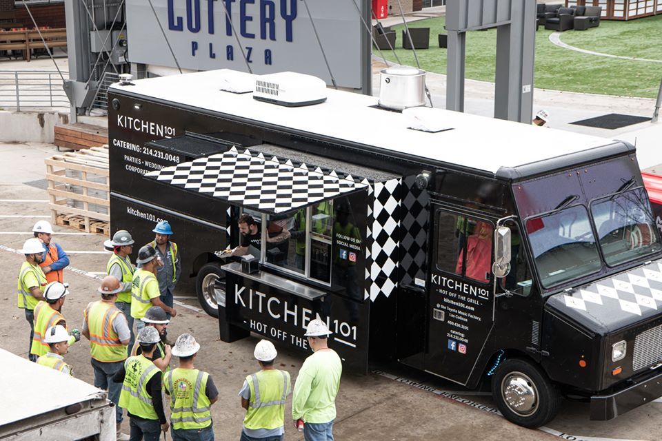 A group of construction workers are standing in front of a black and white food truck.