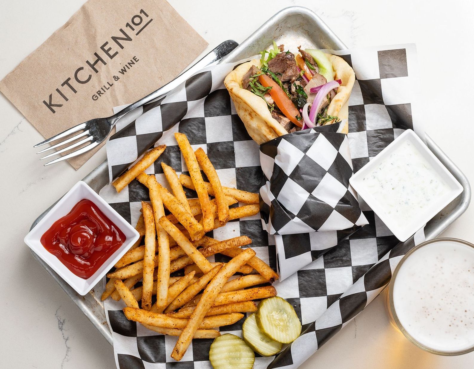 A tray of food with a sandwich , french fries and a glass of beer.