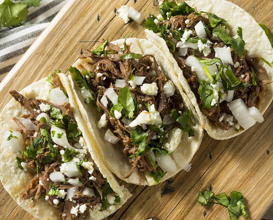 Three tacos are sitting on a wooden cutting board.
