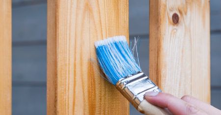 A person is painting a wooden post with a blue brush.