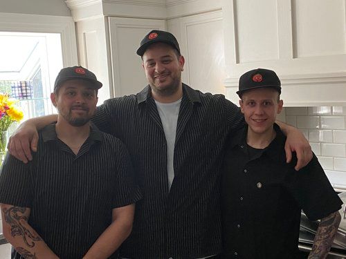 Three men are posing for a picture in a kitchen.