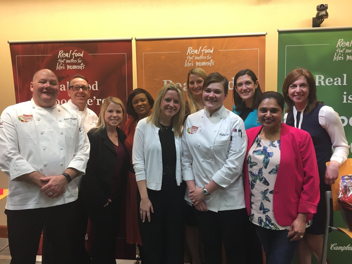 A group of people are posing for a picture in front of a sign that says `` real food is good ''.