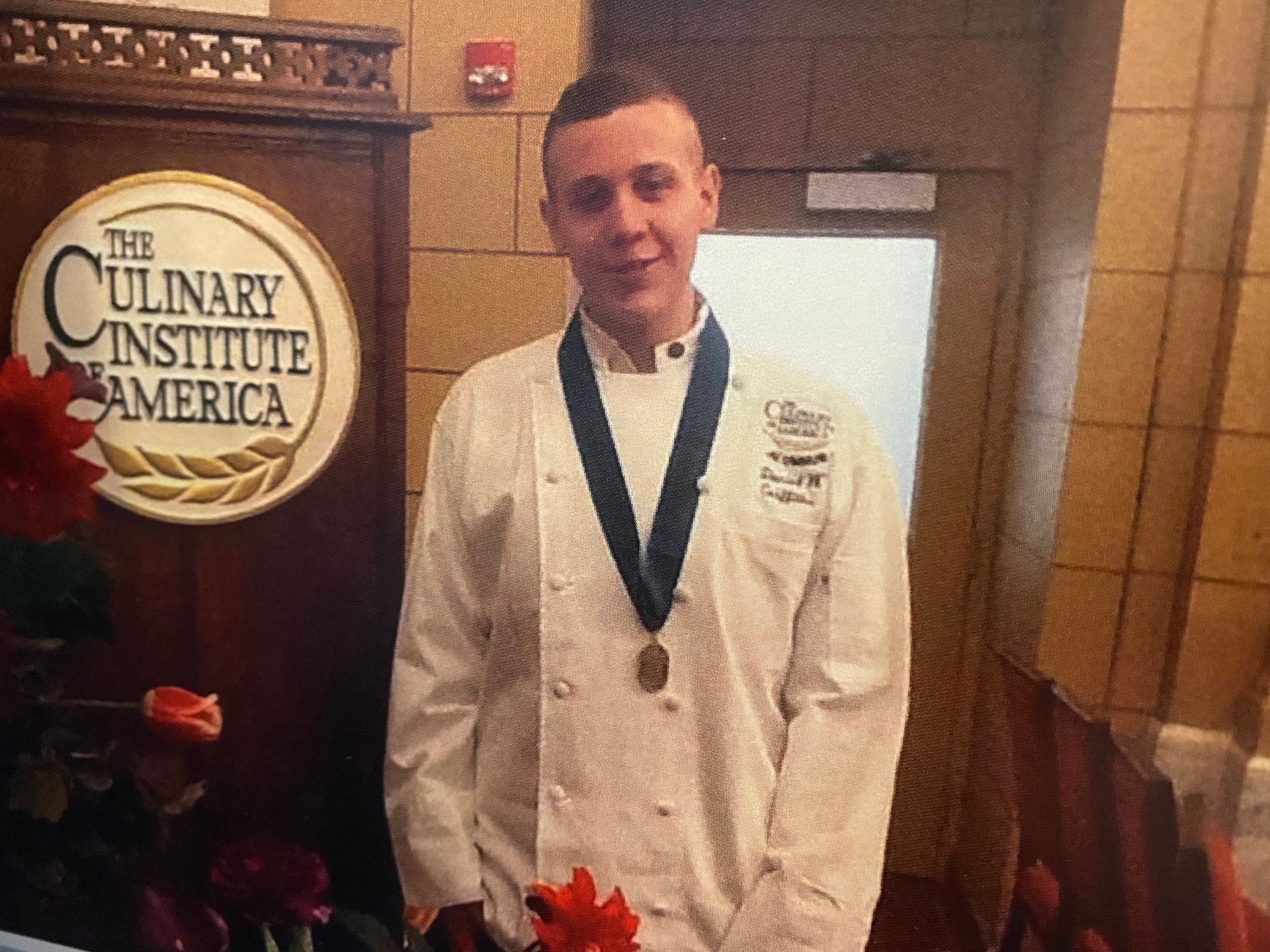 A man wearing a medal is standing in front of a sign that says the culinary institute of america