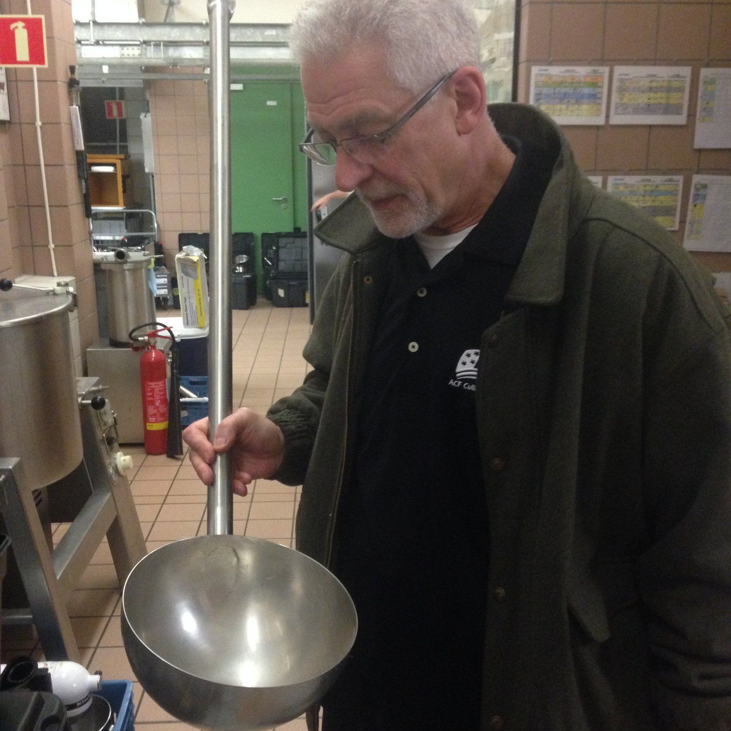A man in a green jacket is holding a ladle in a kitchen