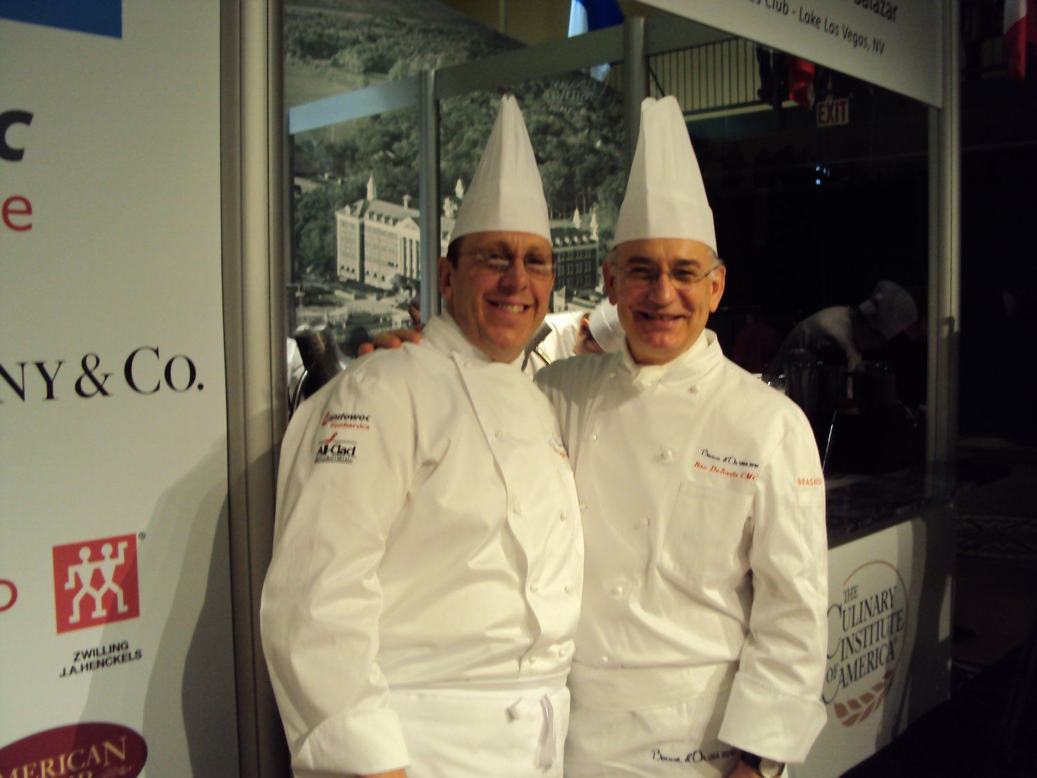 Two chefs are posing for a picture in front of a ny & co. sign