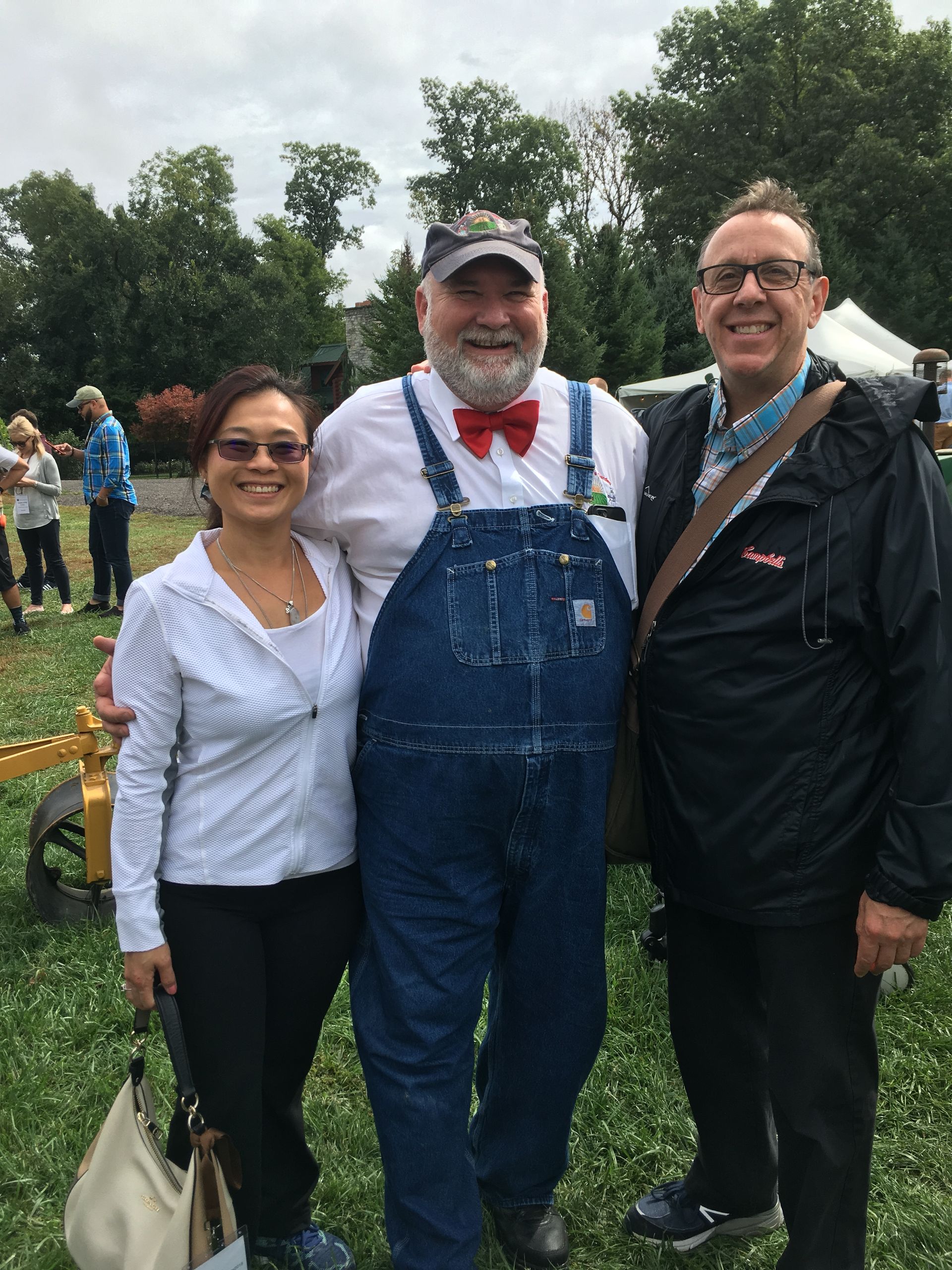 A man in overalls is posing for a picture with two other people.