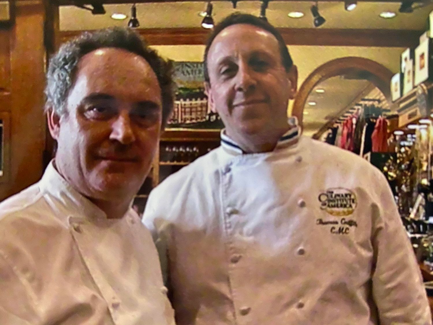 Two men standing next to each other with one wearing a chef 's jacket that says c.m.c.