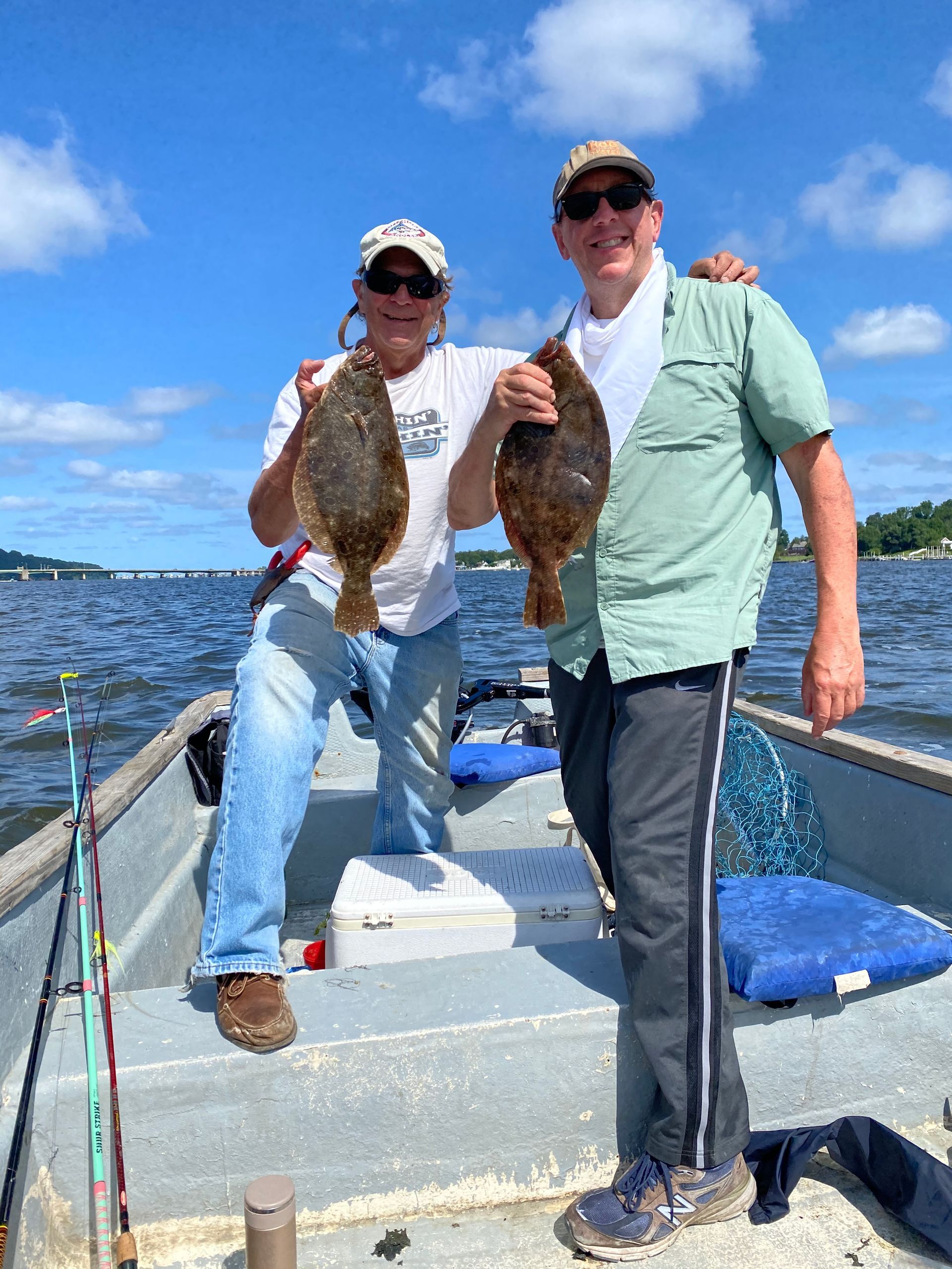 Two men are standing on a boat holding fish.