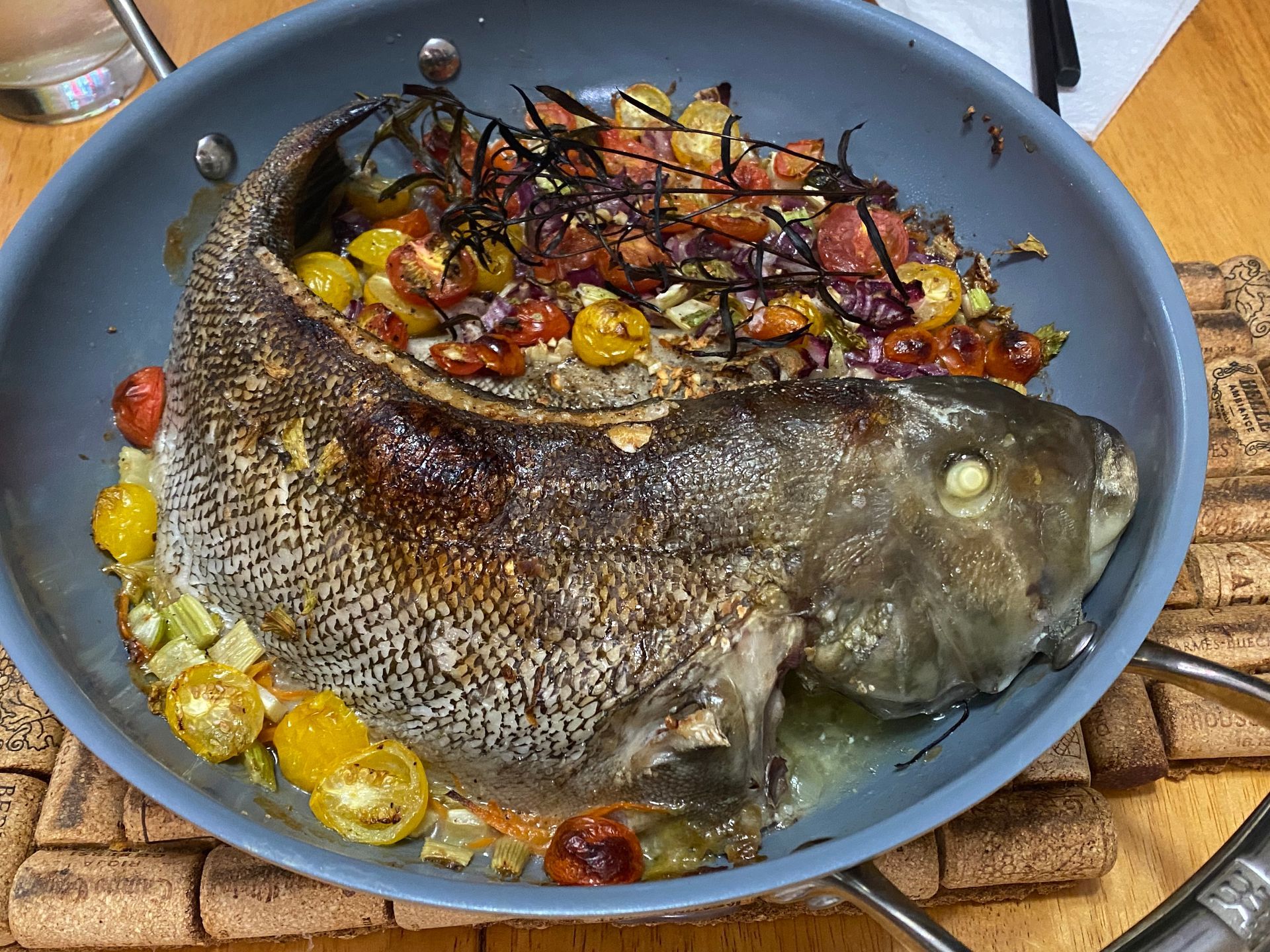 A large fish is being cooked in a pan with vegetables.
