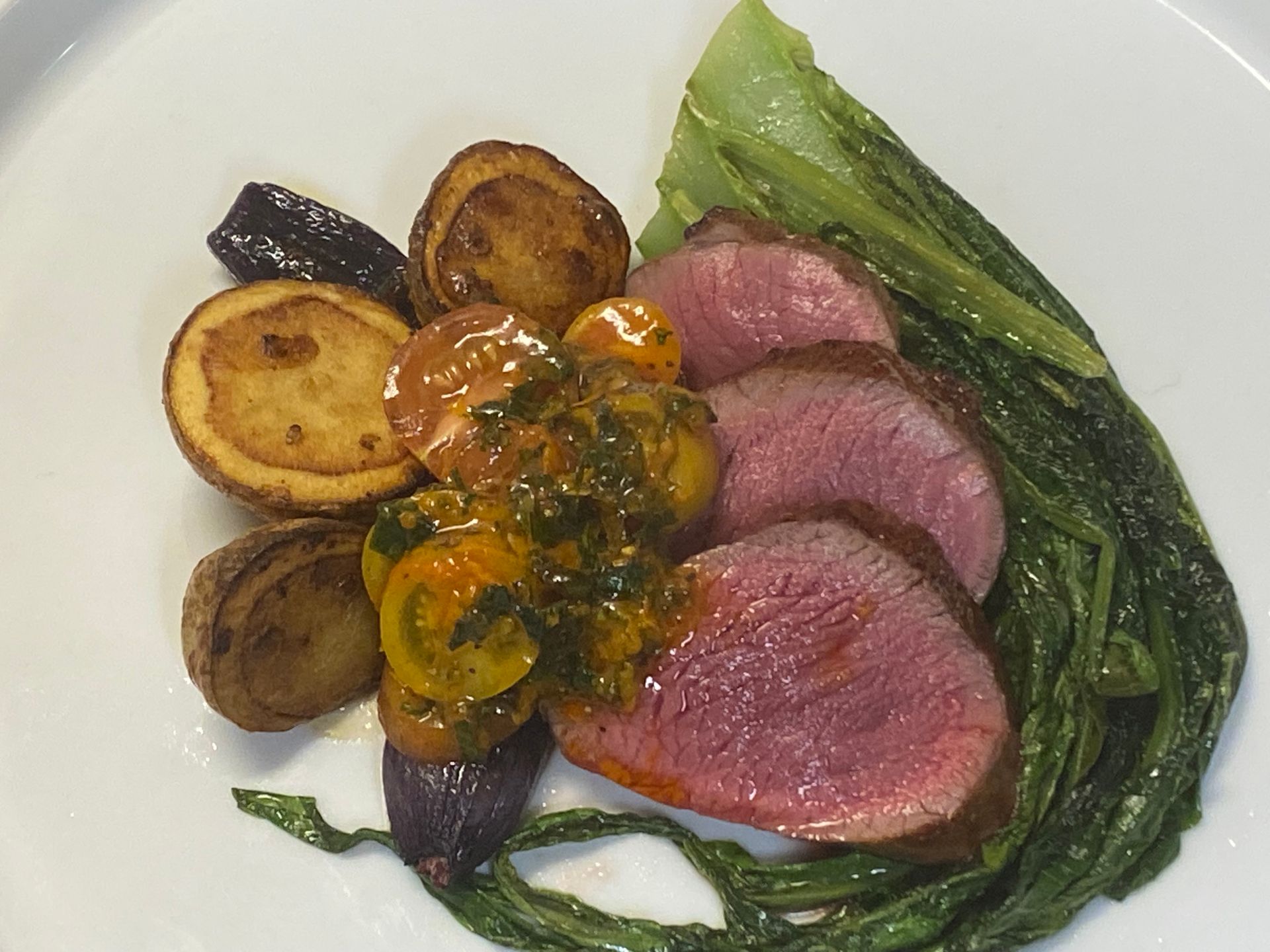 A white plate topped with meat potatoes and greens