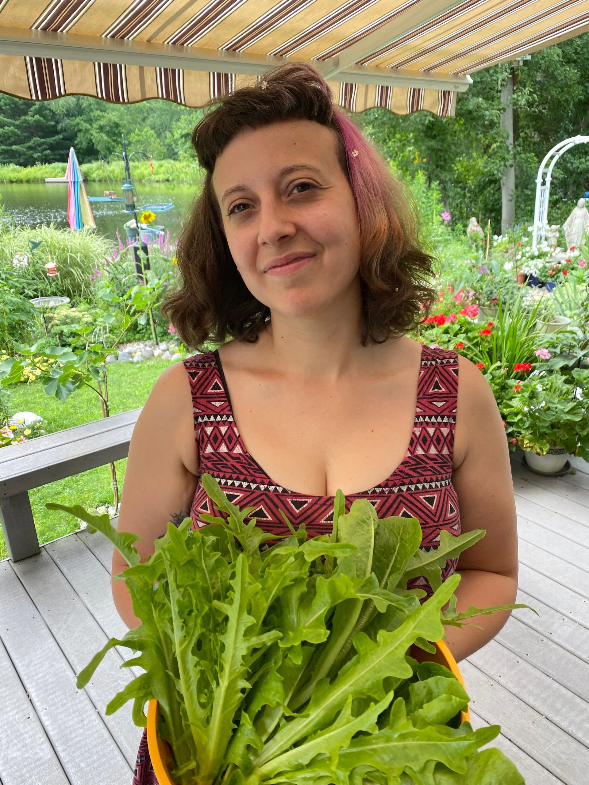 A woman is holding a basket of lettuce on a deck.