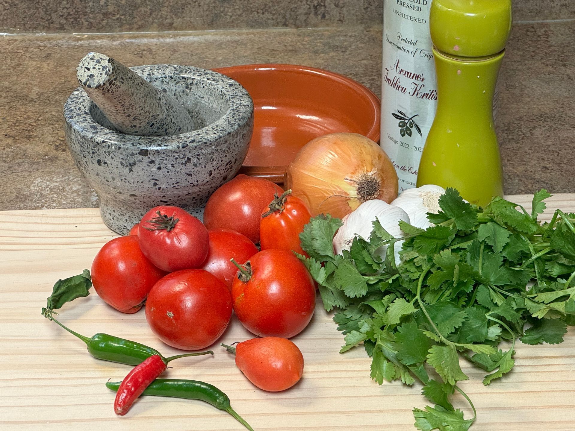Tomatoes , onions , garlic , cilantro , peppers and a mortar and pestle on a cutting board