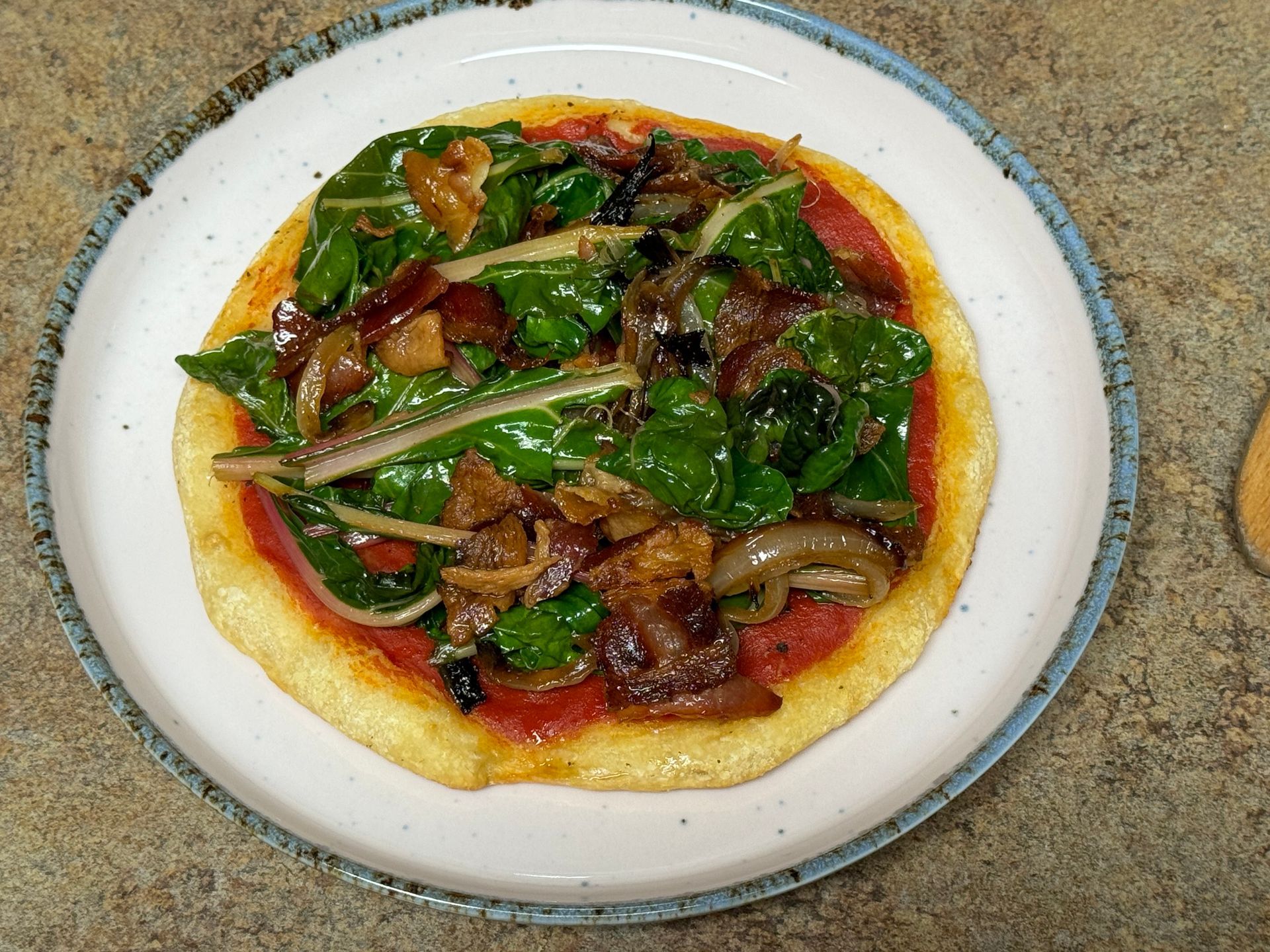 A pizza with spinach and mushrooms on a white plate