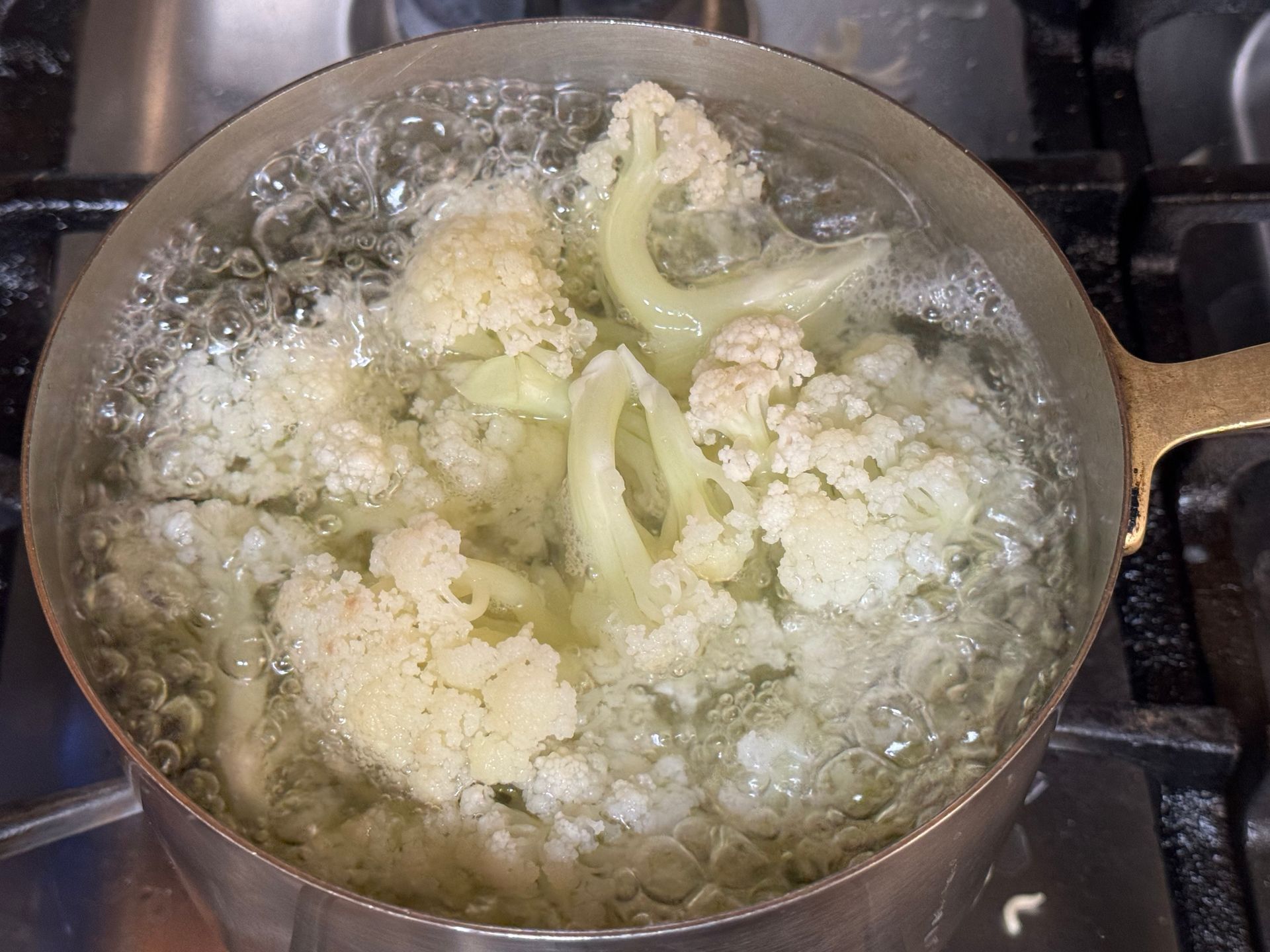 Cauliflower is being cooked in a pot of water on a stove.