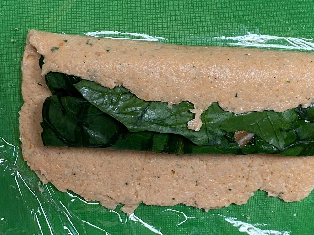 A close up of a sandwich wrapped in plastic wrap on a green surface.