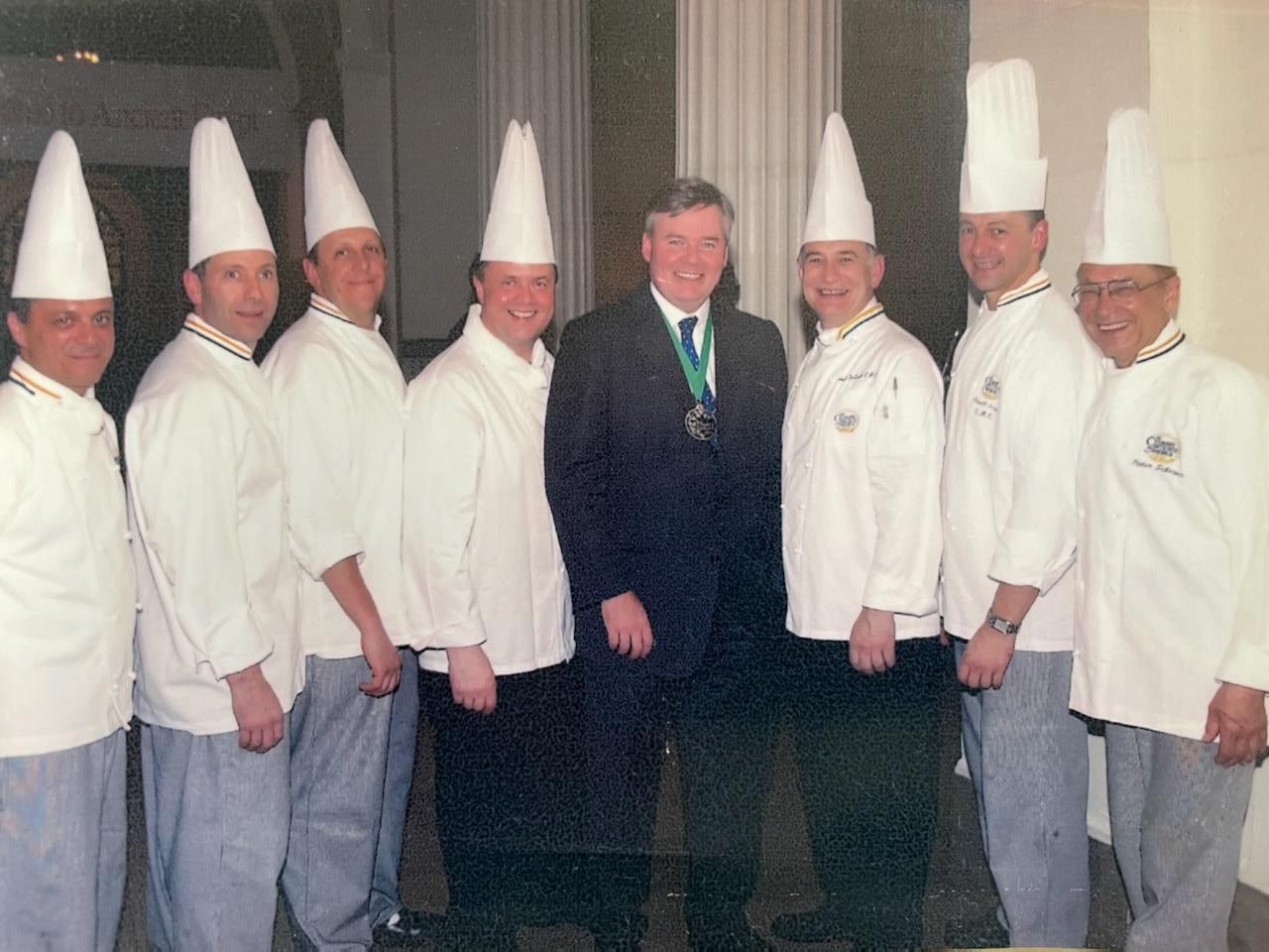 A group of chefs are posing for a picture with a man in a suit