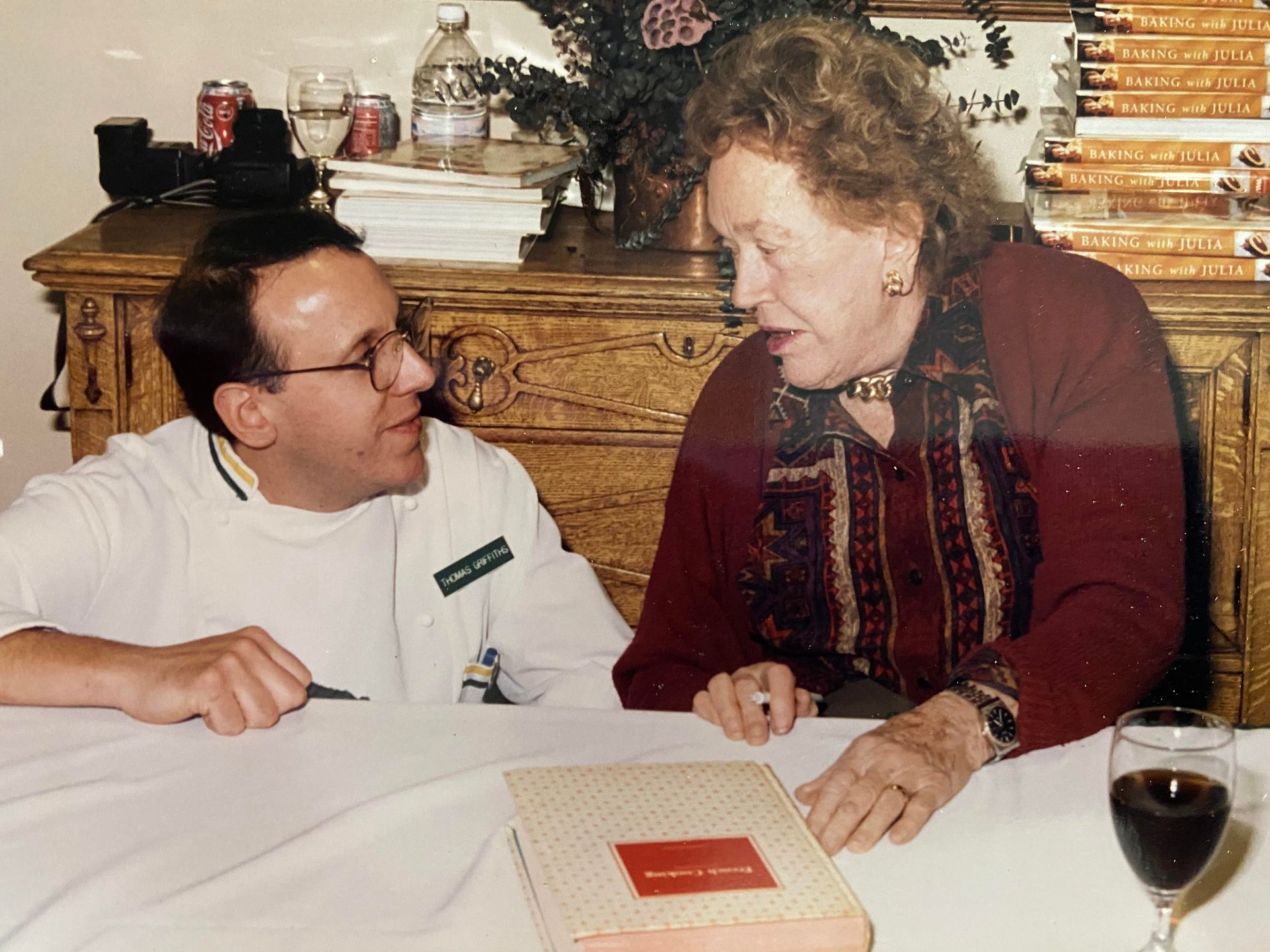 A man and a woman are sitting at a table with a book and a glass of wine