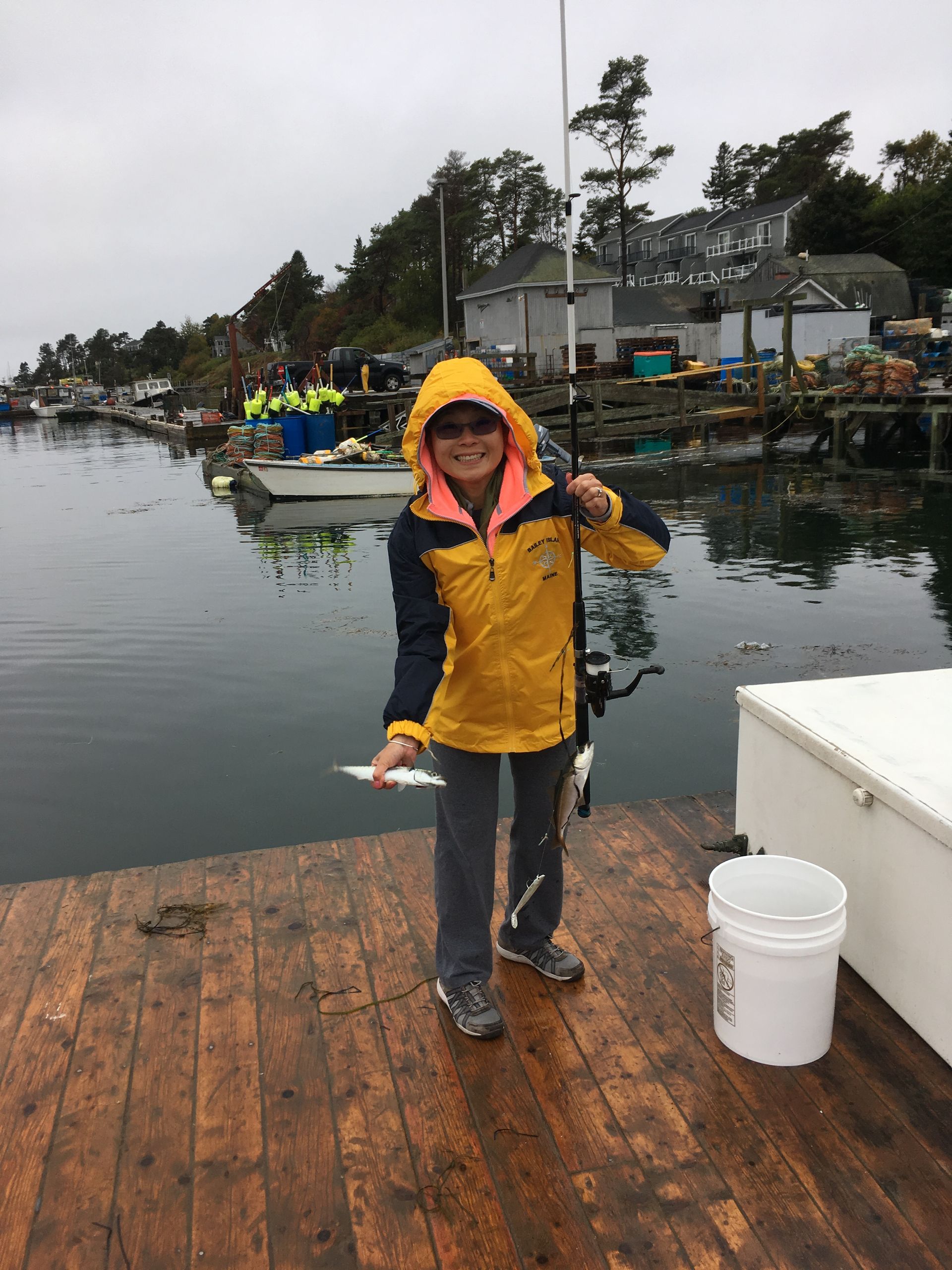 A woman in a yellow jacket is fishing on a dock