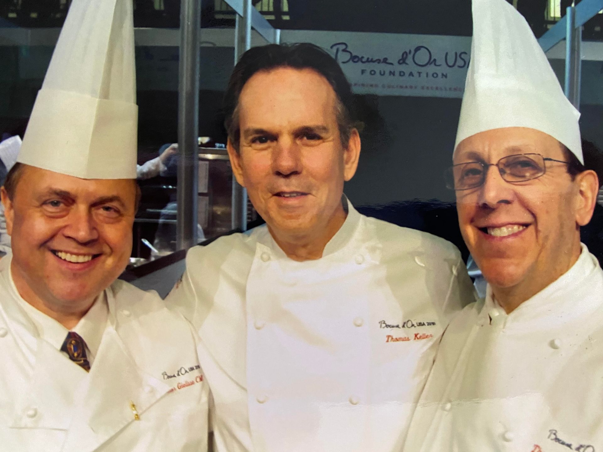 Three men are posing for a picture in front of a sign that says because of us